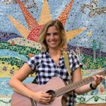 Molly poses with a guitar in front of the mural at Paul's Run.