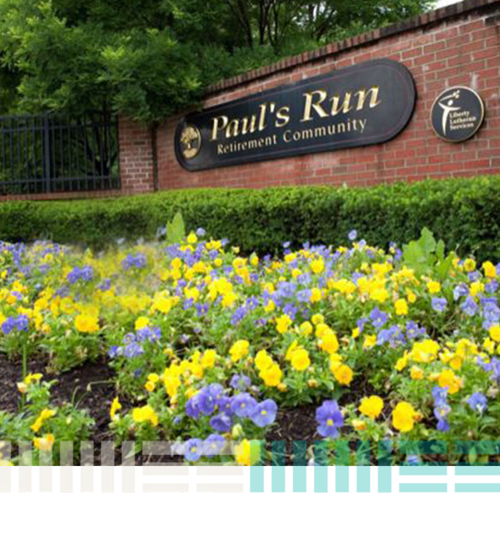 sign welcoming visitors to Paul's Run Retirement Community , with yellow and purple flowers in the foreground