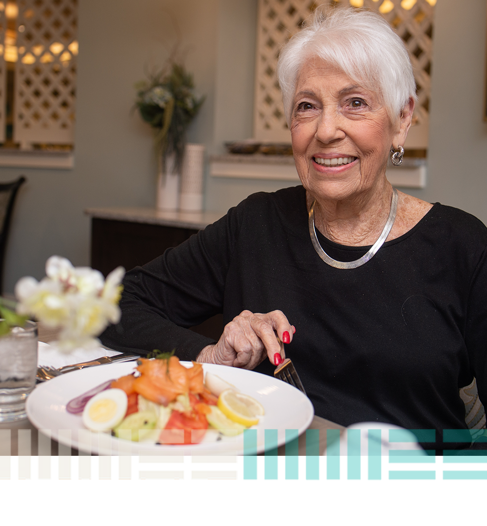 a happy resident smiles for the camera before enjoying a delicious salad on the plate in front of her
