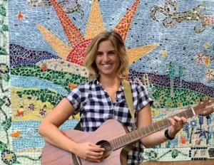A woman strums an acoustic guitar in front of a mosaic wall at Paul's Run Retirement Community in Northeast Philadelphia